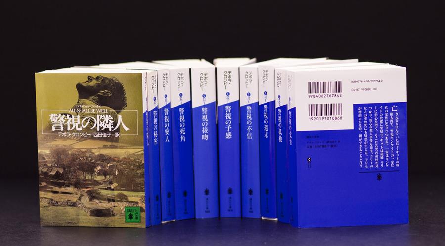 A row of blue and white books seen from the spine and extended out. The book on the furthest left has a back cover that is near brown in color.