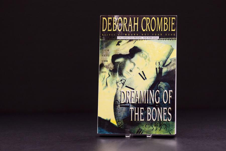 The front cover of a book with the name Deborah Crombie on it in yellow lettering. The title Dreaming Of Bones is on the bottom right side, with a man also on the cover.