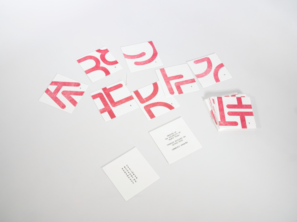 A set of square cards with parts of letters printed in red ink on each in a pattern design, with a small black version of the letter on each card.