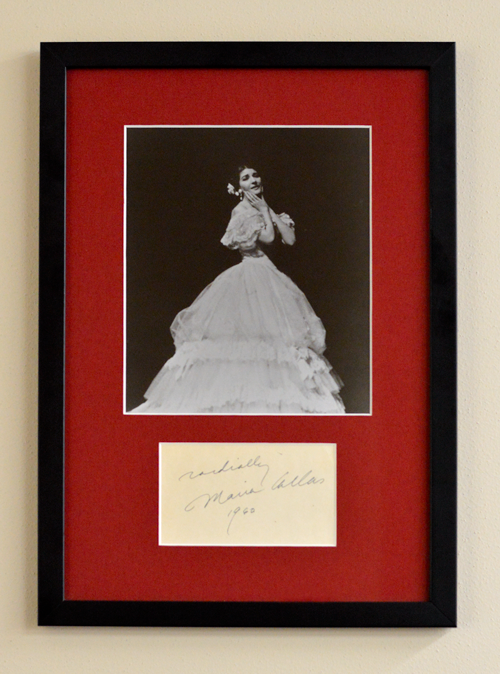 Una foto en blanco y negro de una mujer con un gran vestido y una flor en el pelo. La foto está sobre un fondo rojo, todo ello en un marco negro.