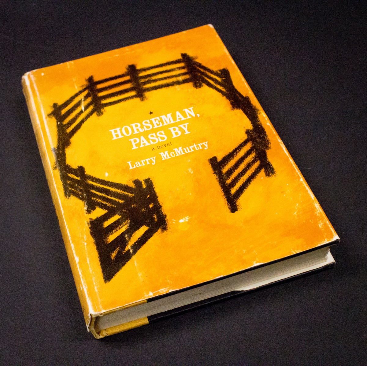 Un libro amarillo con una ilustración de una valla circular marrón. El título del libro está en el centro en letras blancas, con el autor Larry McMurtry debajo en letras blancas.
