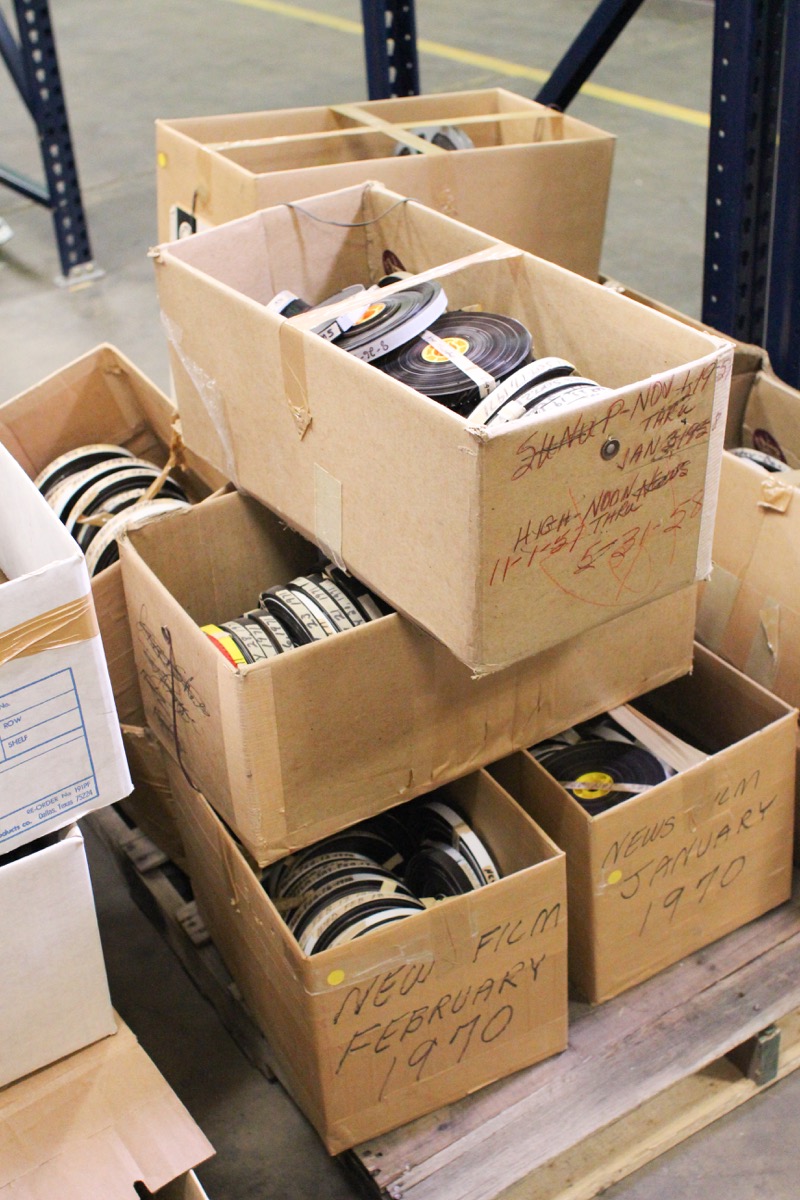 Boxes on top of each other are shown, with film reels inside of them. The boxes are filled up with the reels, with old marks on the outside of it.