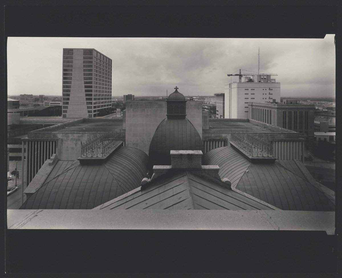 Black and white photo from a rooftop. It overlooks several other rooftops of buildings downtown.