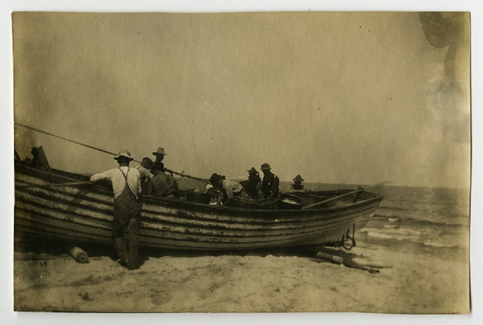Old photo of men on a long boat, left on land.