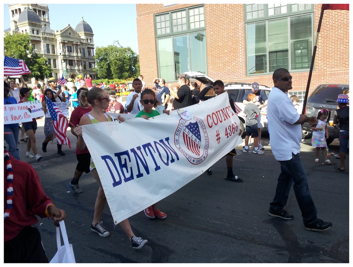 Personas marchando por una calle, con un cartel que dice "Condado de Denton".